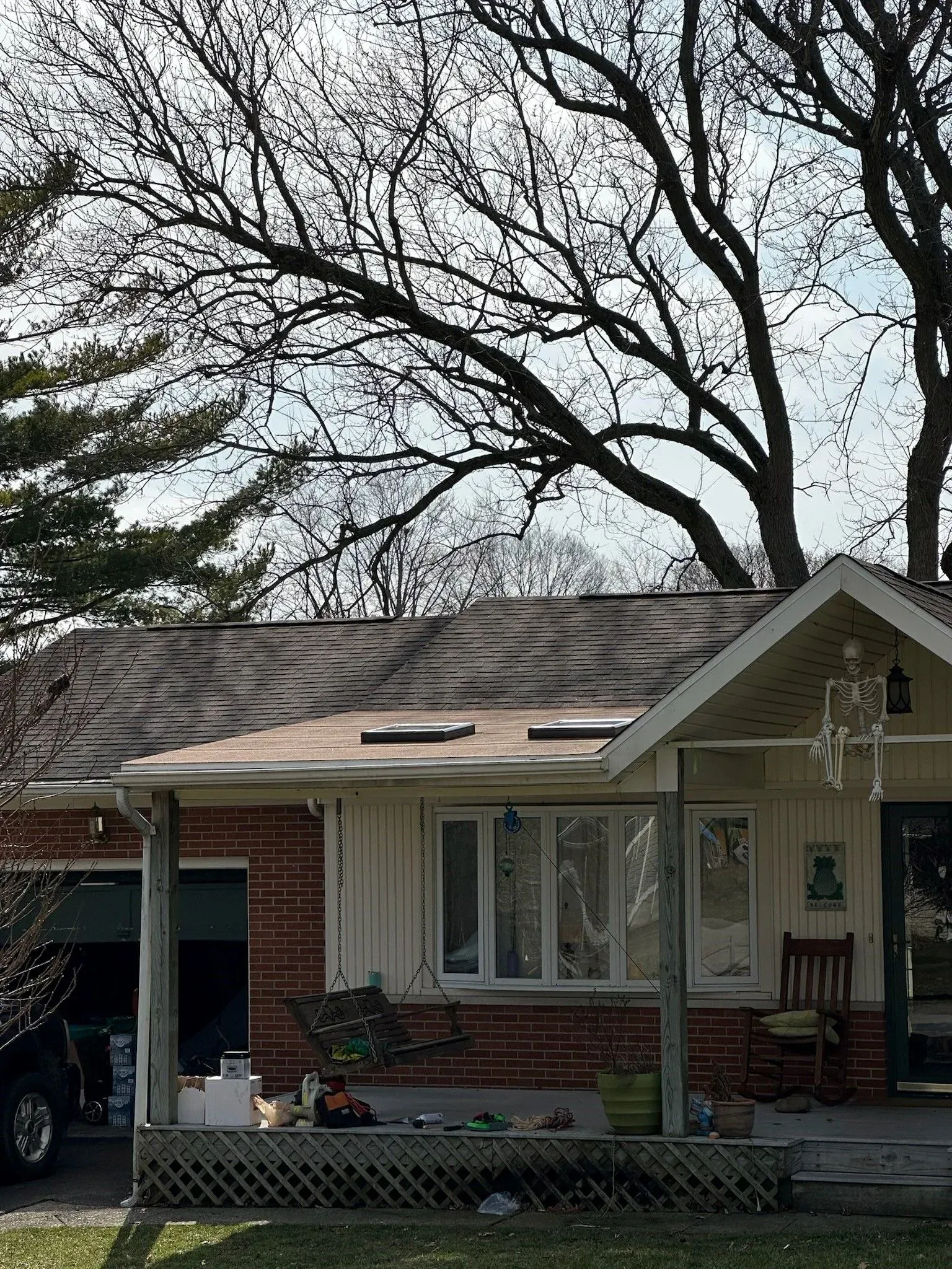 A one-story brick house with a porch and bare trees in the background. Skeleton decoration hangs.