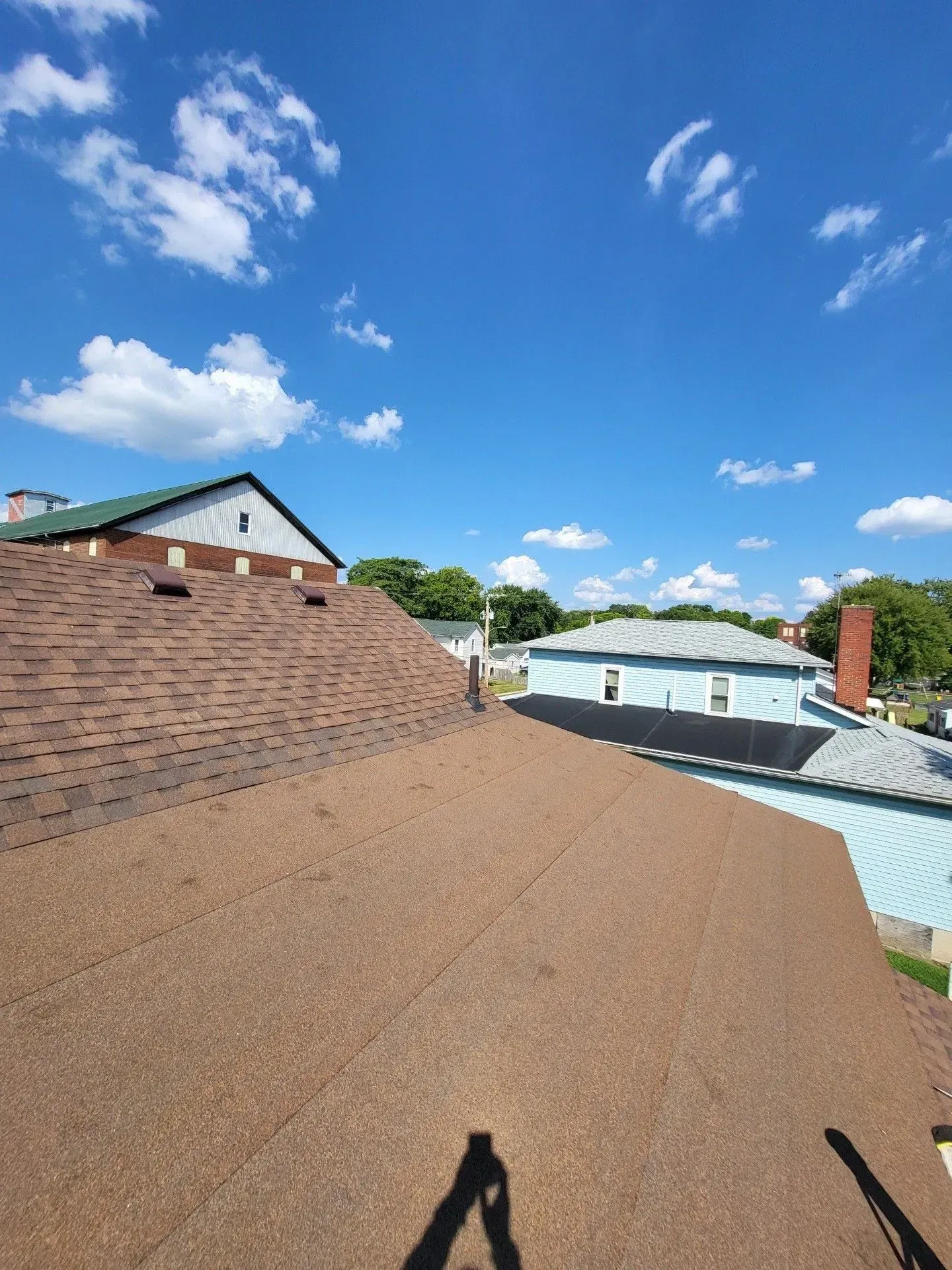 Brown shingled roof with a clear blue sky and fluffy clouds in the background.