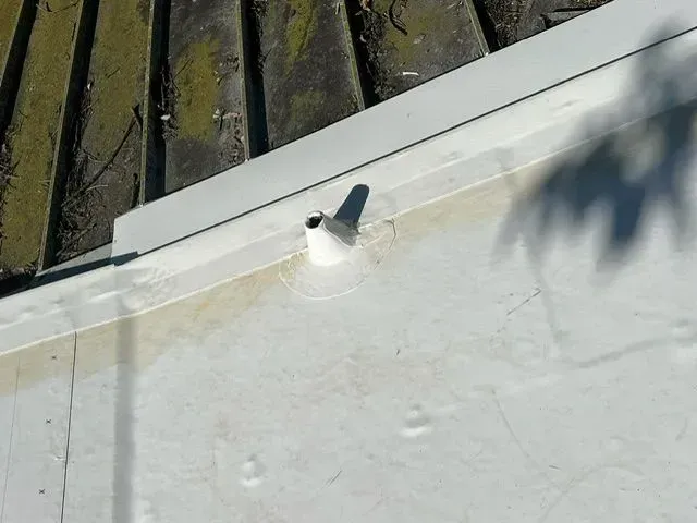 White roof drain protruding from white membrane, next to a metal edge and corrugated roof.