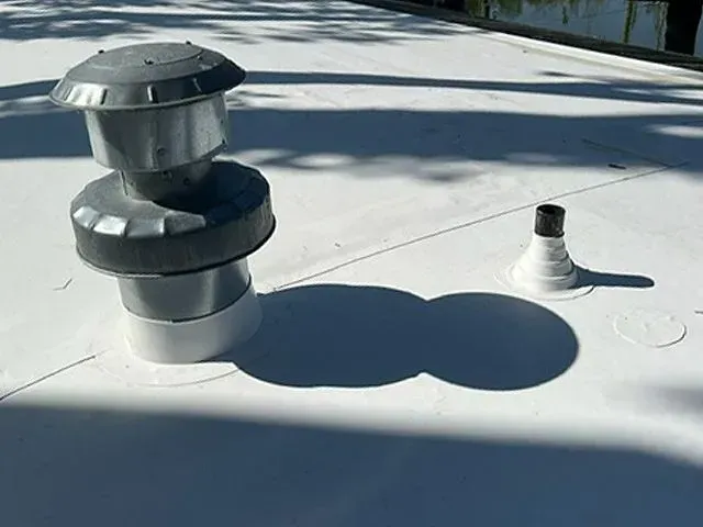 Two roof vents on a white flat roof. One vent is larger with a metal cap, the other is smaller.