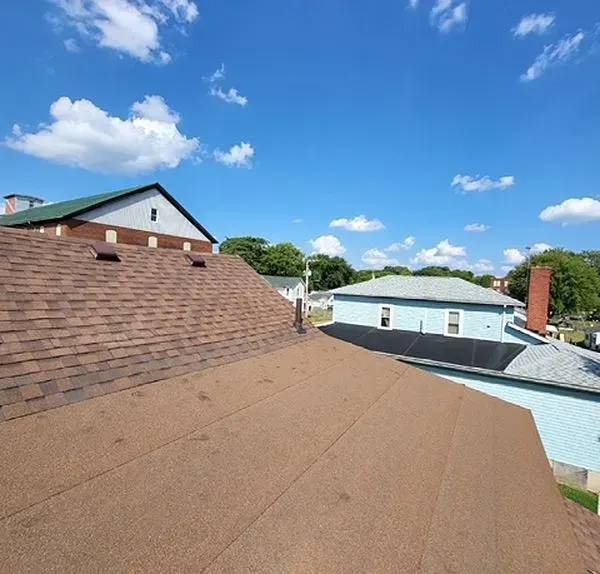 Brown shingled roofs against a blue sky with fluffy clouds. Houses with green and blue paint are in the background.
