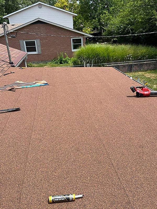 Brown, flat roof with cork-like material; brick house in background. A leaf blower and screwdriver are on the roof.