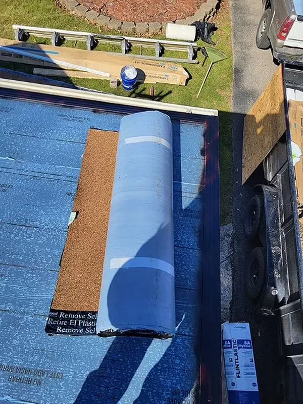 Blue roofing material roll on a partially covered roof with brown shingles.