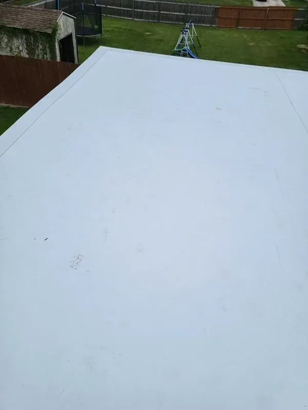 Flat, light-colored roof of a building with a backyard view featuring green grass and a small shed.