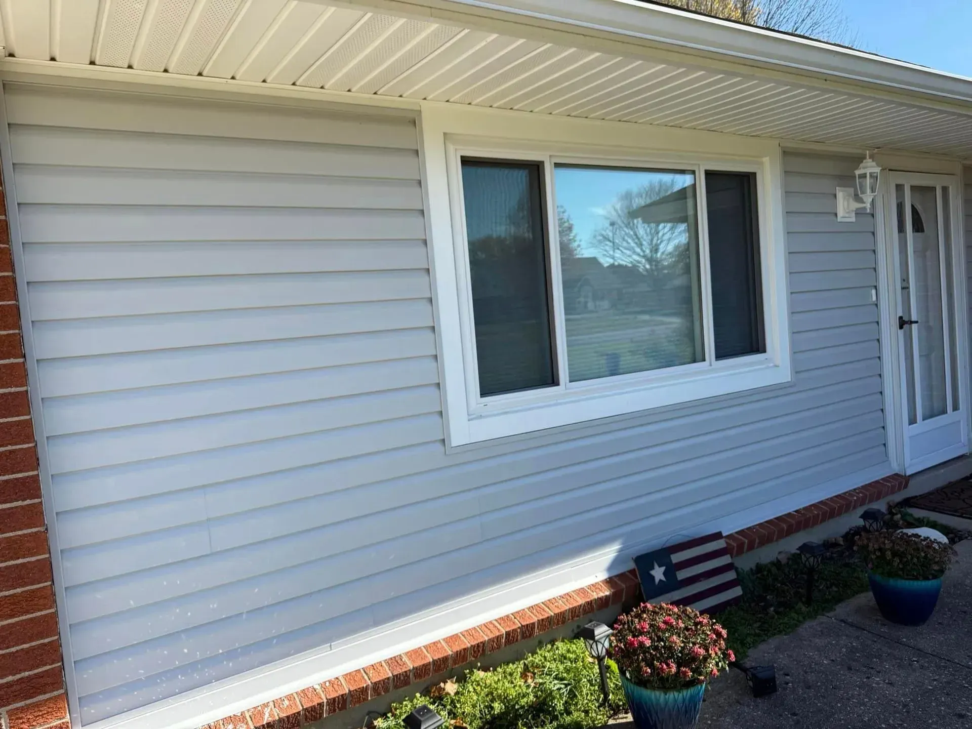 Light blue siding on a house with a window, white trim, and a brick base.