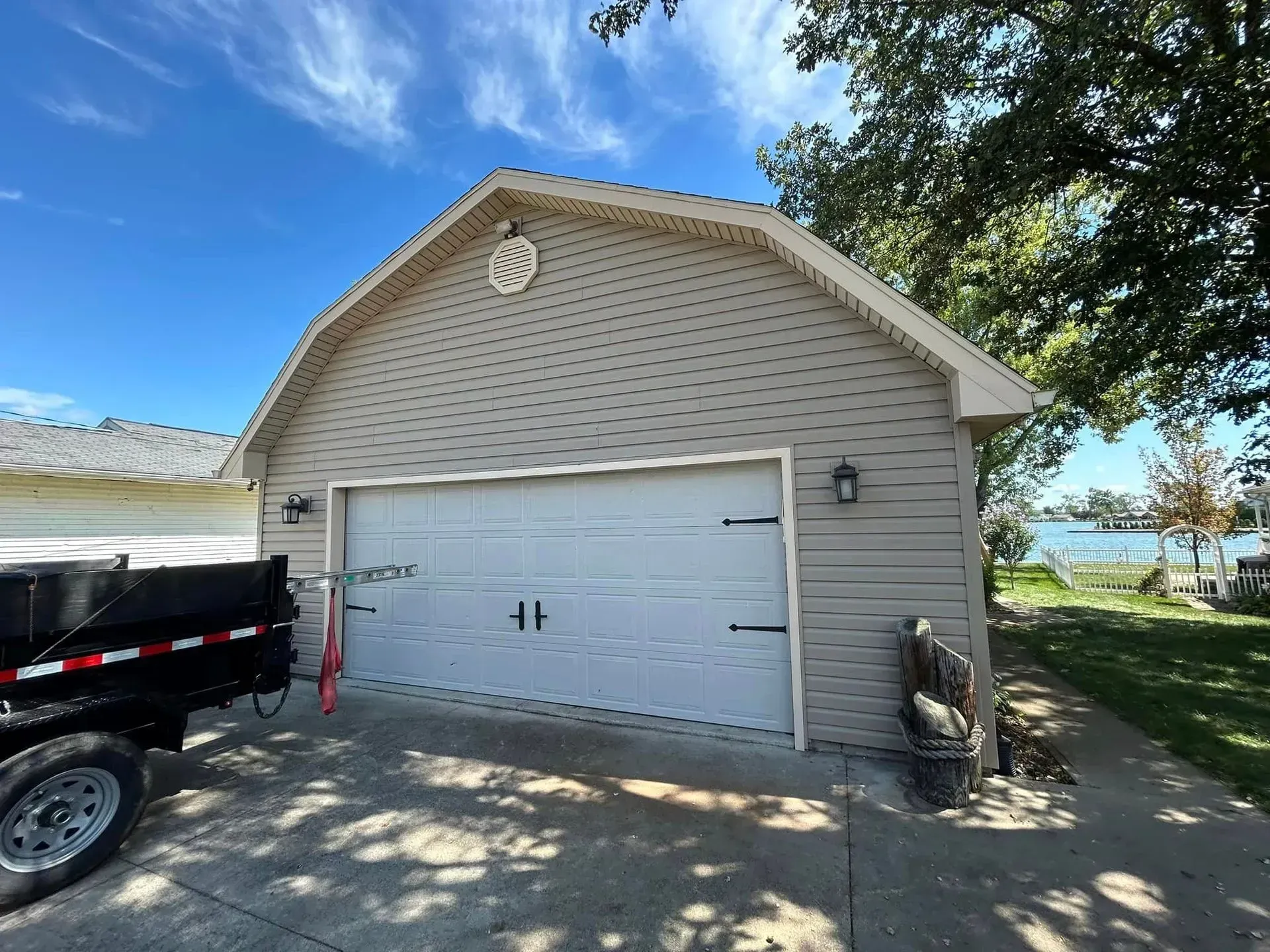 Tan garage with white door, black hardware, and two sconces, set under a blue sky near water.