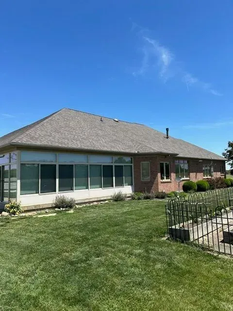 A brick house with a glass-walled sunroom and green lawn under a bright blue sky.