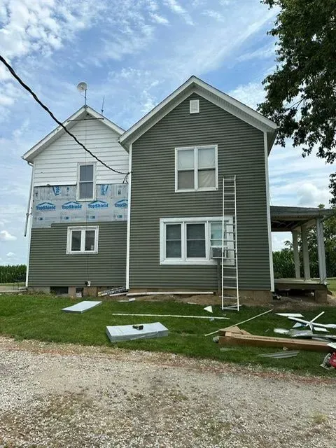 House with new green siding. Partially completed, old white siding still exposed, ladder present.