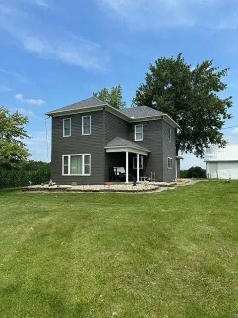 Two-story gray house with white trim on a grassy field under a blue sky.