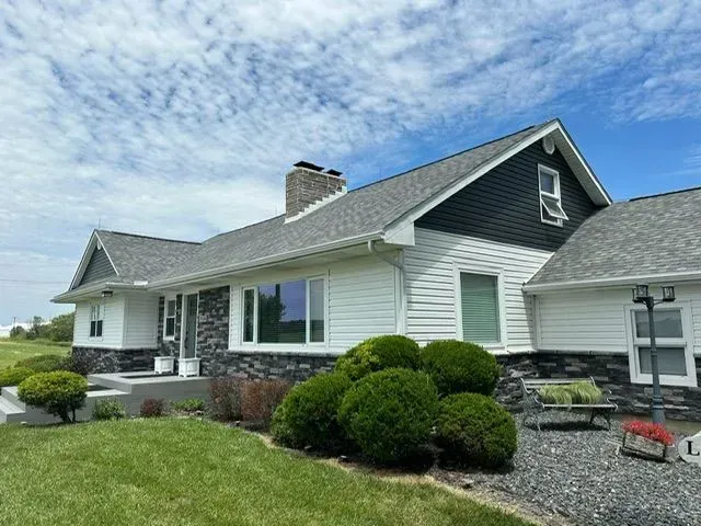 House with gray roof and black and white siding, green bushes, and blue sky.