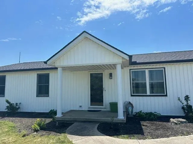 White house with black trim, porch, and dark roof under a blue sky.