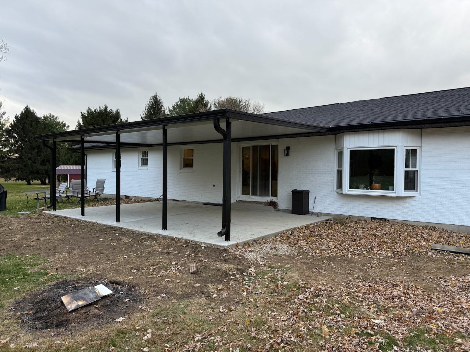 Black-framed patio cover attached to a white brick house, over a concrete patio.