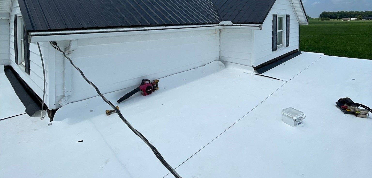 A person is using a leaf blower on a white flat roof of a white house.