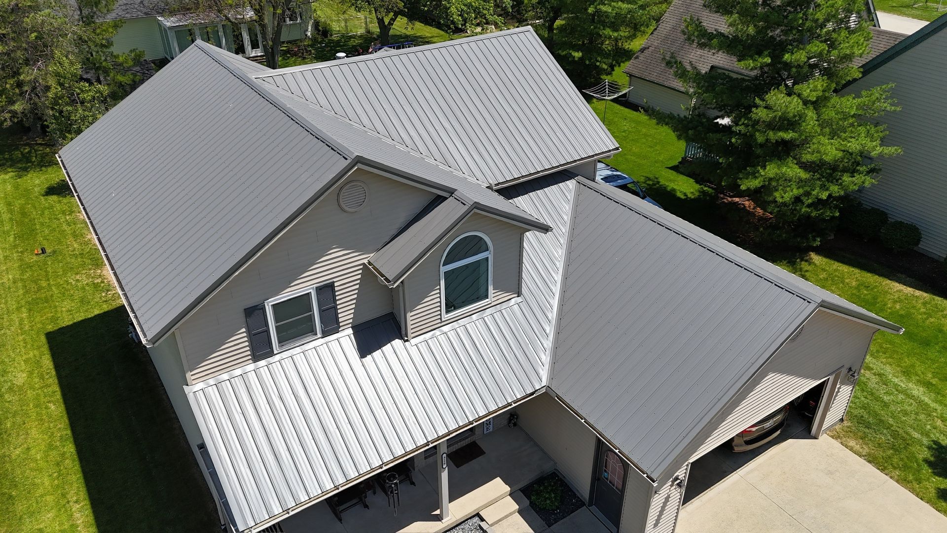 Gray metal roof on a two-story house with beige siding and a garage, viewed from above.