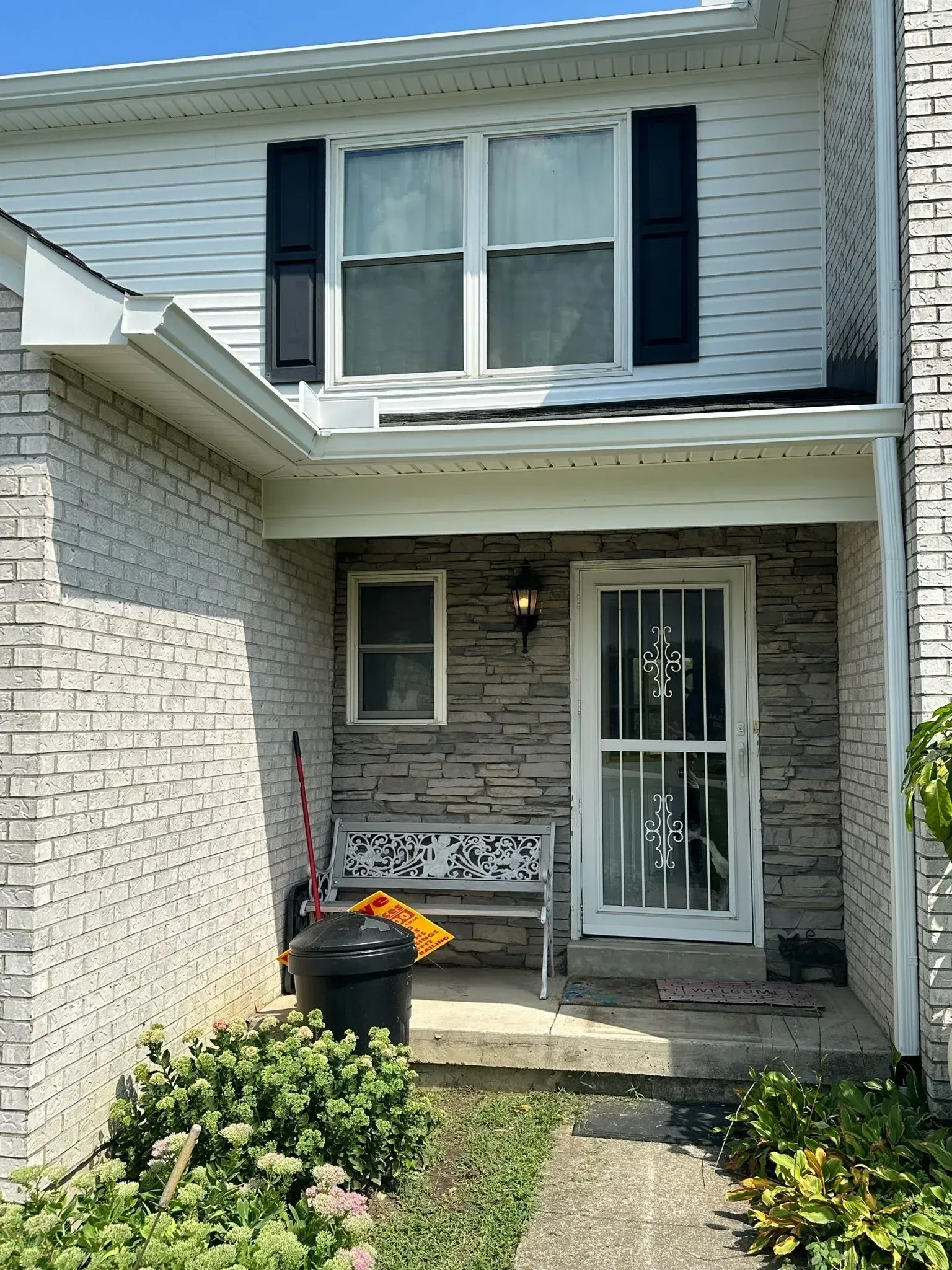 Exterior view of a home entrance with a brick façade, front door, small window, and a bench.