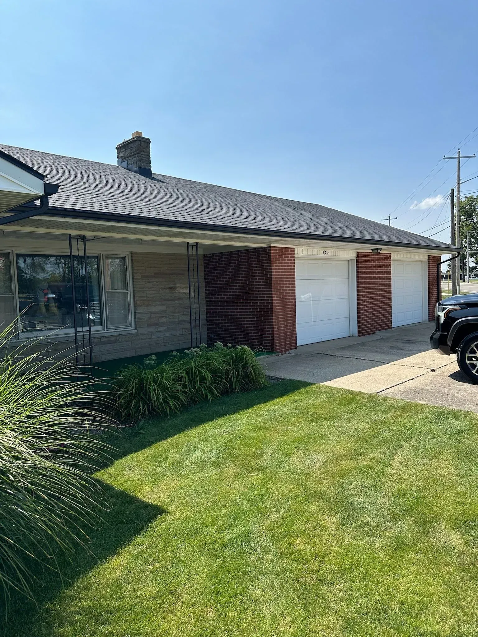 A ranch-style house with a brick facade and dark roof has two garage doors and a green lawn on a sunny day.