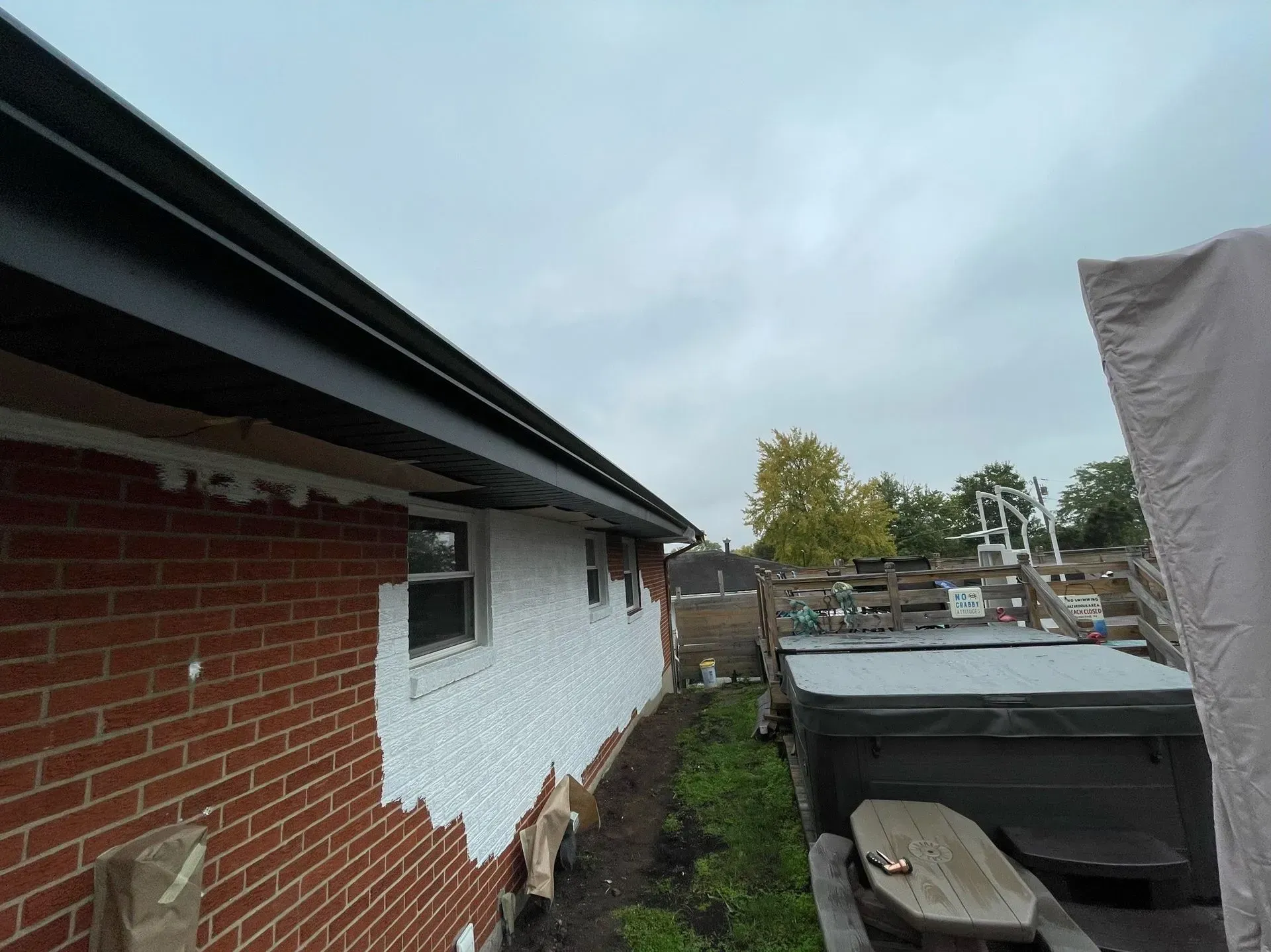 Side of a brick house with black trim, partially covered in white stucco, cloudy sky.