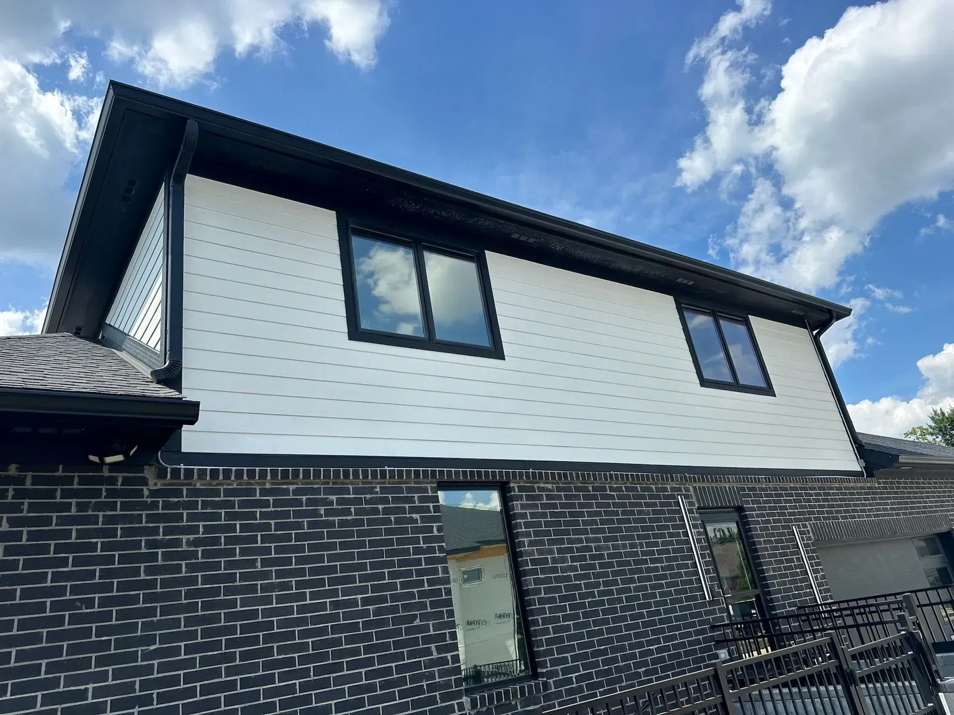 Black and white exterior of a building with brick and white siding, black trim, and windows, against a blue sky.