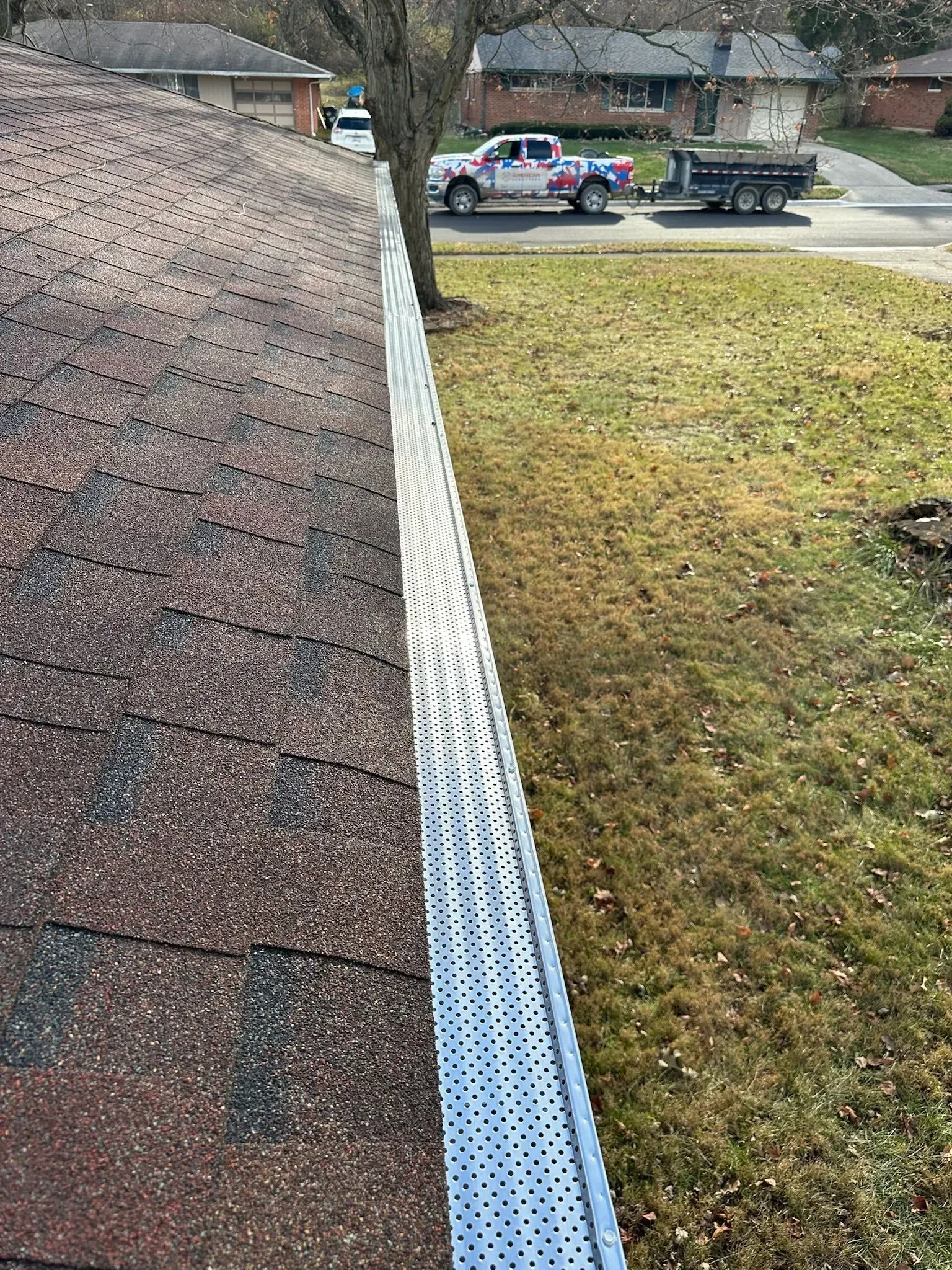 A roof with leaf guards next to a grassy area with a truck and trailer in the background.