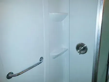 White shower stall with grab bar, shelves, and showerhead.