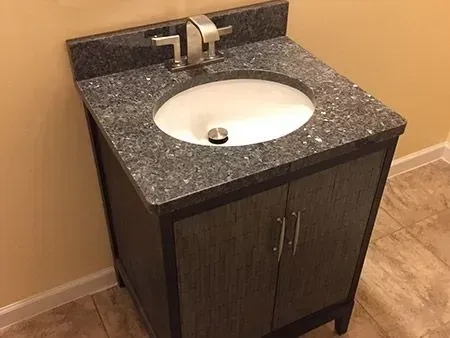Bathroom vanity with granite countertop and oval sink, set against a beige wall.