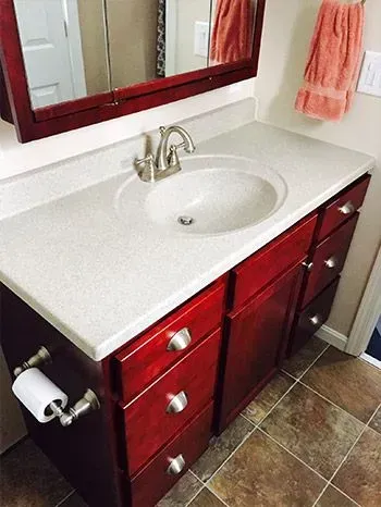 Red bathroom vanity with a white countertop and a round sink, and a roll of toilet paper on the side.