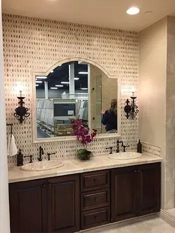 Bathroom with a double vanity. Dark wood cabinets, oval sinks, ornate mirror, patterned tile backsplash, and sconces.