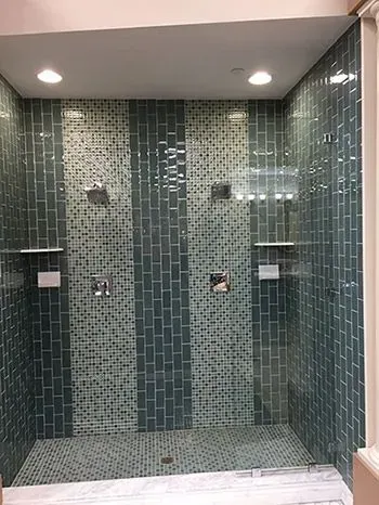 Blue tiled shower with dual showerheads, shelves, and a glass door.