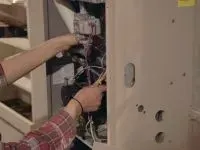 Person in red plaid shirt working on electrical wiring inside a furnace.