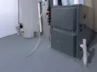 Gray furnace and water heater in a basement with gray flooring.