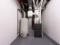 A basement utility room with a water heater, furnace, and ductwork. Grey floor, white walls.