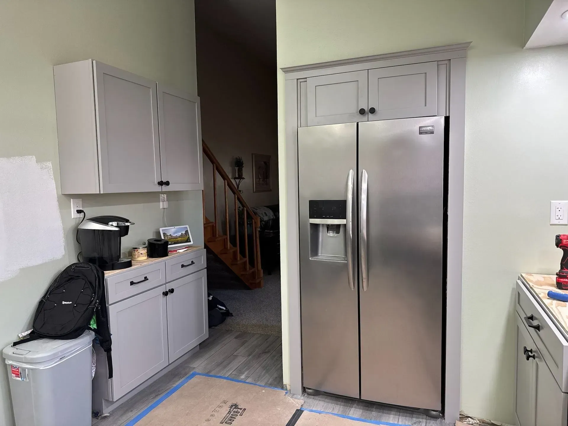 Kitchen with gray cabinets, stainless steel refrigerator, and a staircase visible in the background.