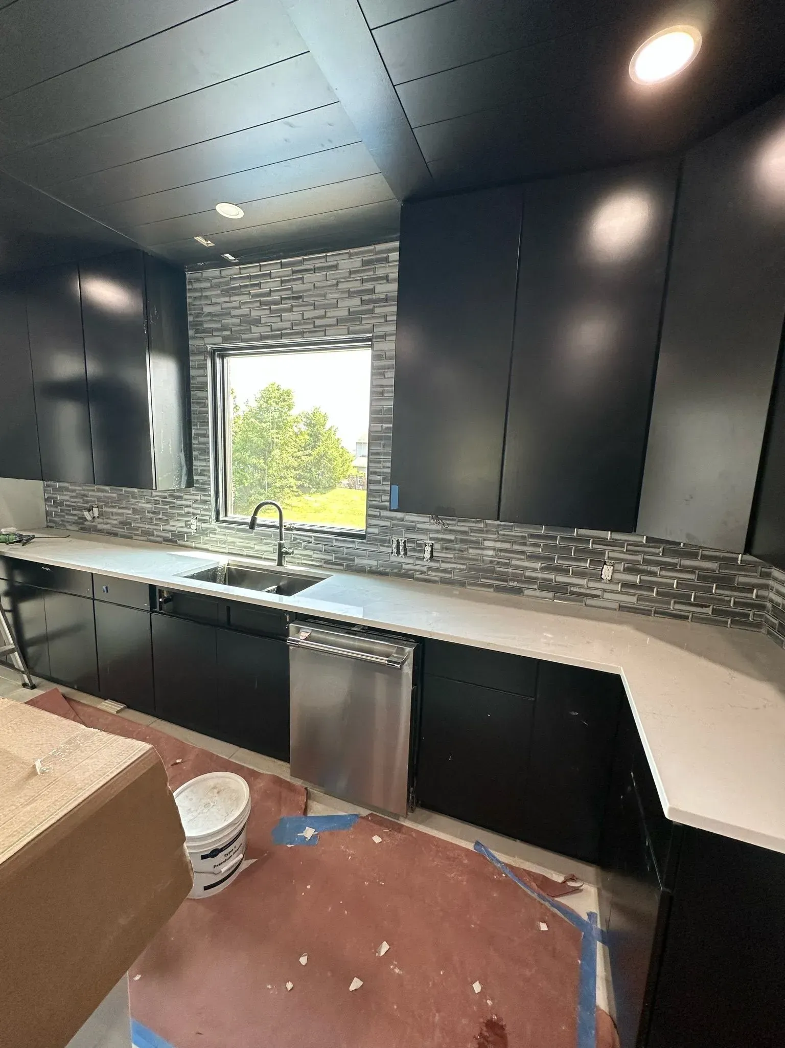 Modern kitchen with black cabinets, white countertops, stainless steel appliances, and a mosaic tile backsplash.