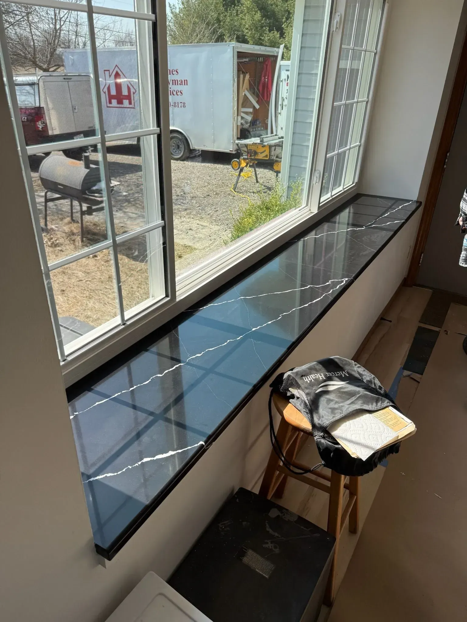 Window with a long black countertop, a stool with a backpack, and a black chest.