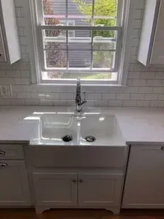 White farmhouse-style kitchen sink under a window. Subway tile backsplash, cabinets below.