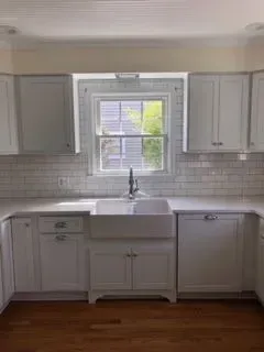 White kitchen with farmhouse sink, cabinets, window, and subway tile backsplash.