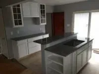 Modern kitchen remodel with white cabinets, dark countertops, island with sink, and sliding glass door.