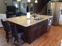 Kitchen island with granite countertop, dark cabinets, sink, and bar stools.