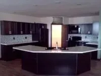 Dark wood kitchen with a large island and light-colored countertops. Backsplash with small mosaic tiles.