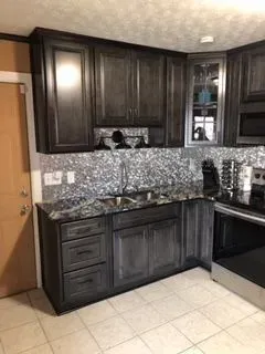 Kitchen with dark gray cabinets, granite countertop, mosaic backsplash, and stainless steel appliances.