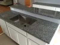 Kitchen island with gray granite countertop, stainless steel sink, and white cabinets.