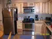 A kitchen with stainless steel appliances, light wood cabinets, and a blue rug.
