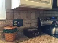 Kitchen counter with appliances: a stovetop, and two decorative containers with a backsplash and electrical outlet.