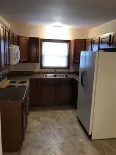 Kitchen with dark brown cabinets, a window above the sink, and a white refrigerator.