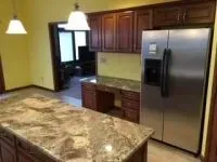 Kitchen with granite island, dark wood cabinets, stainless steel refrigerator, and desk area.