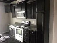 Dark-cabinetted kitchen with stainless steel appliances. Black countertops, white oven, and microwave.