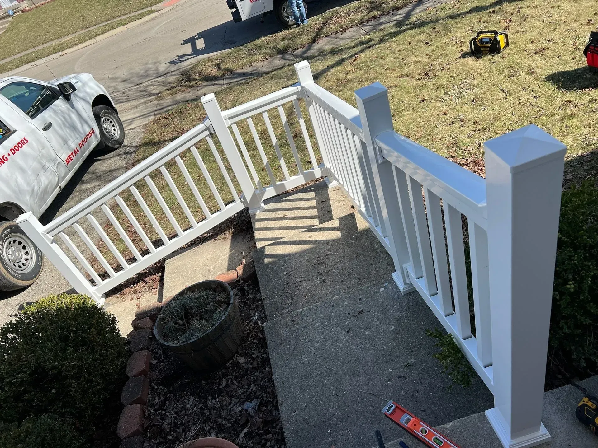 White handrail on concrete steps, near a parked work truck and tools.