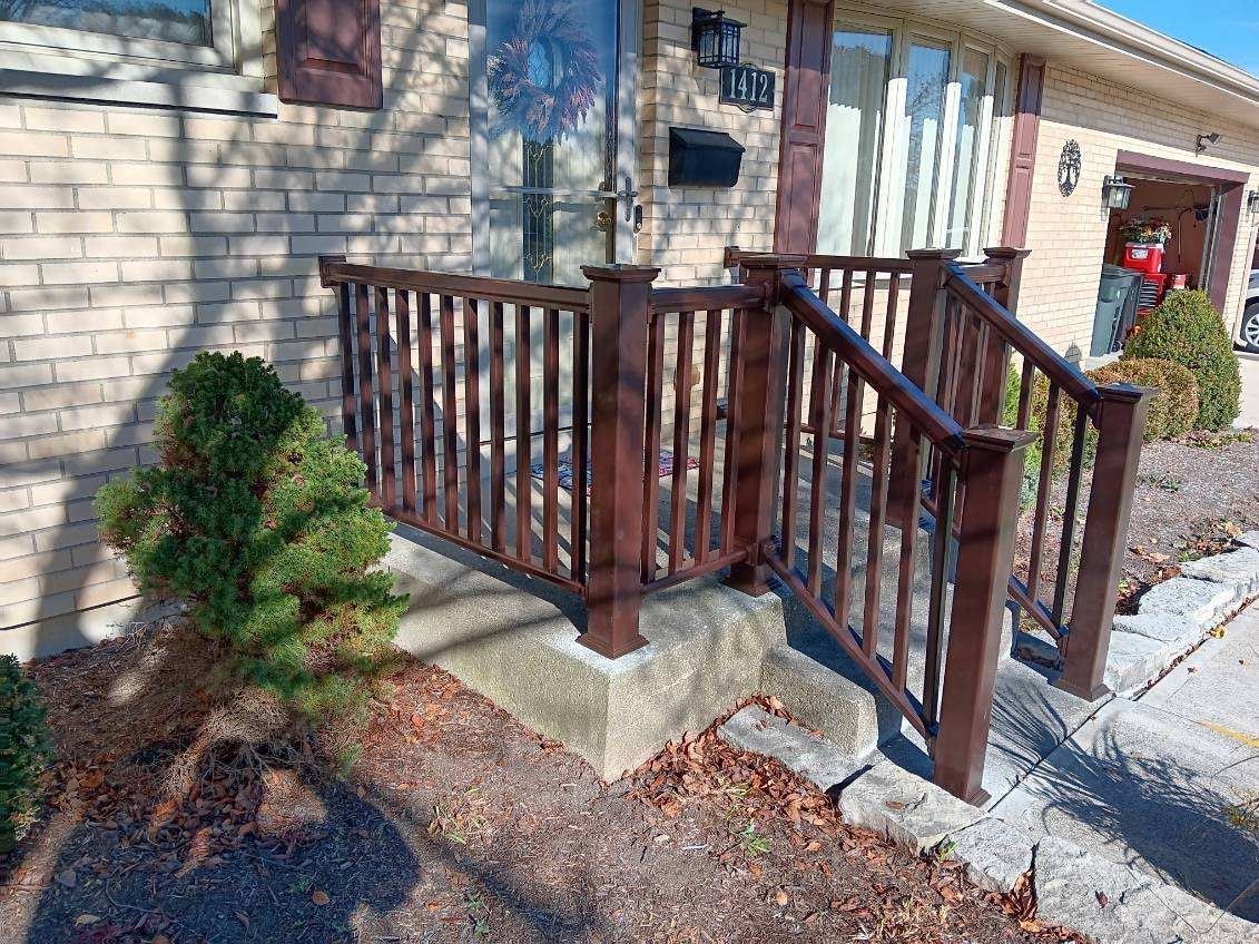 Brown wooden handrail and railing on concrete steps leading to a brick house entrance.