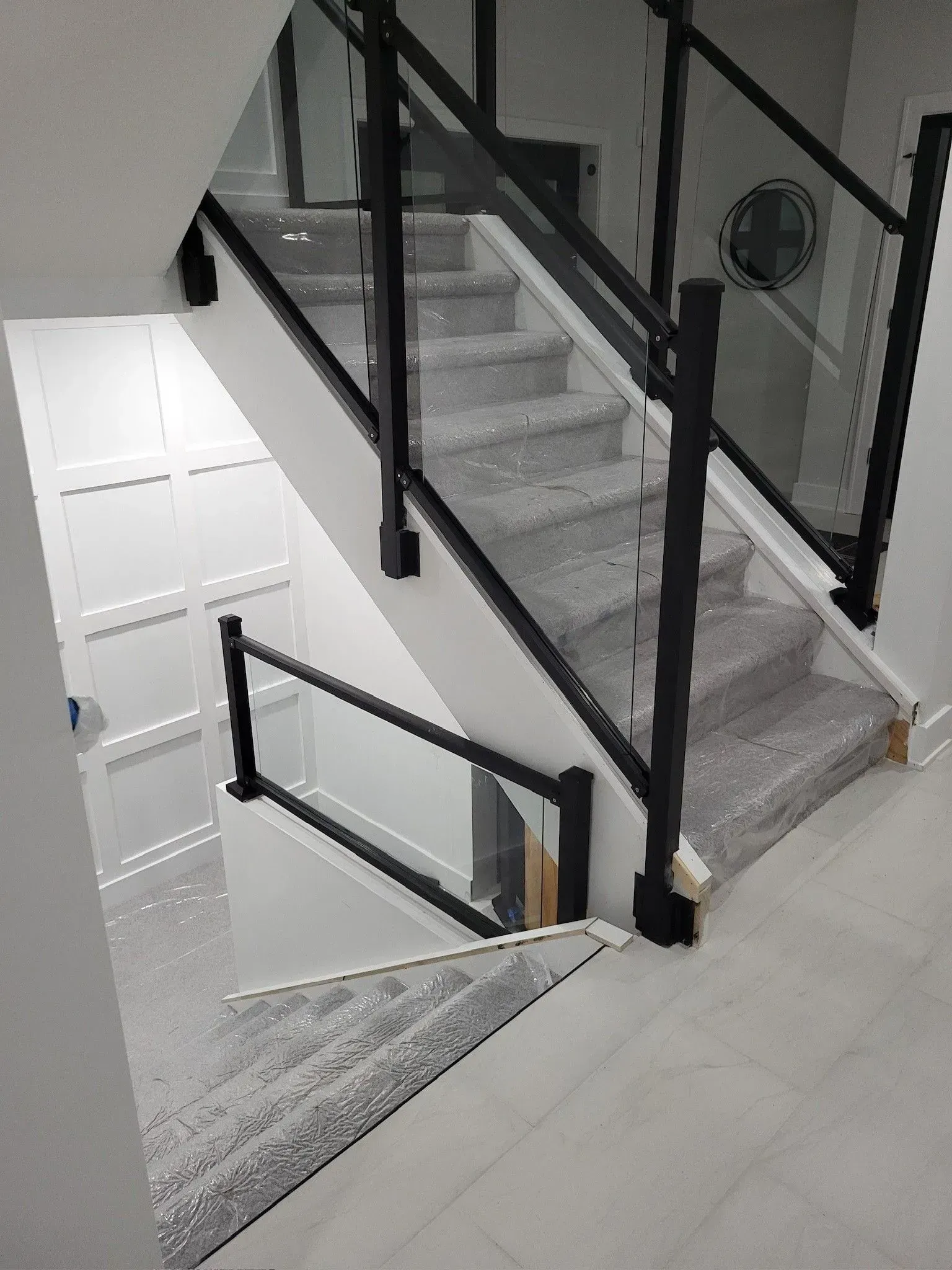 Staircase with glass and black metal railing. White walls, grey carpeted stairs.