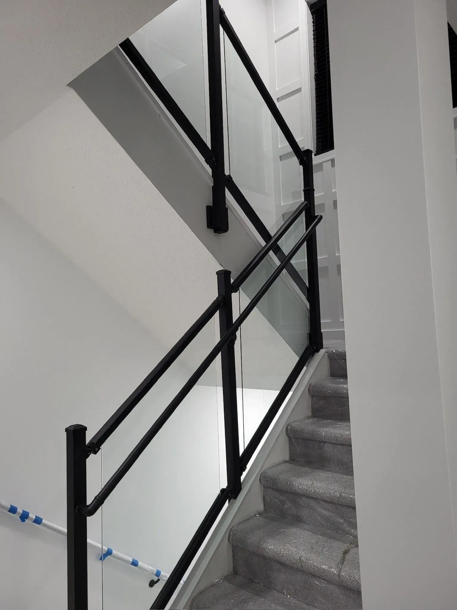 Staircase with black metal railing and glass panel, grey carpet steps, white walls.